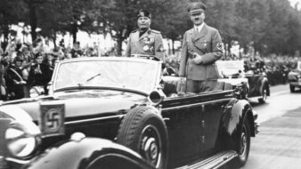 Benito Mussolini, símbolo do fascismo, e Adolf Hitler, símbolo do nazismo, passeiam de carro por Berlim. A população os festeja nas ruas.